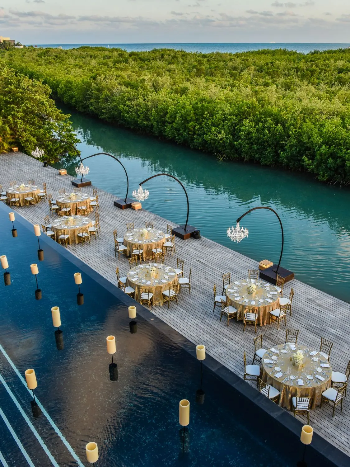 Luxury wedding reception tables set on a waterfront deck overlooking a tranquil lagoon.