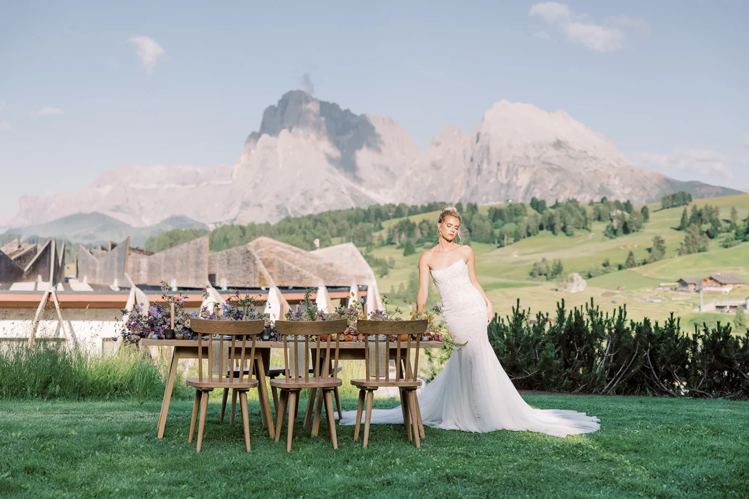 Bride in a wedding dress poses near a rustic table decorated for a styled shoot against a mountain backdrop.