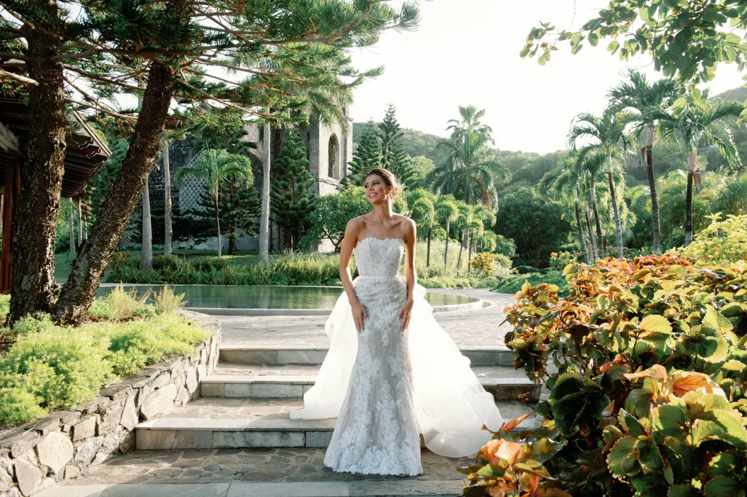 Bride in lace wedding gown poses in tropical garden