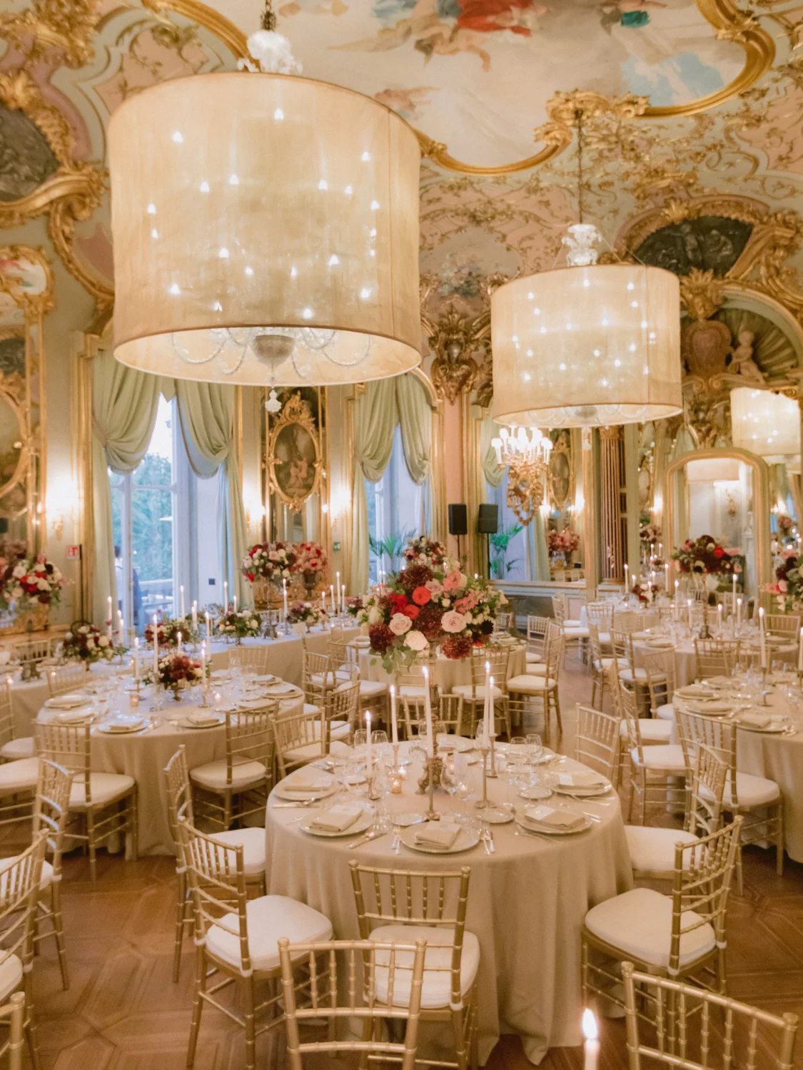 Elegant wedding reception in a grand ballroom with gold chairs and floral centerpieces.