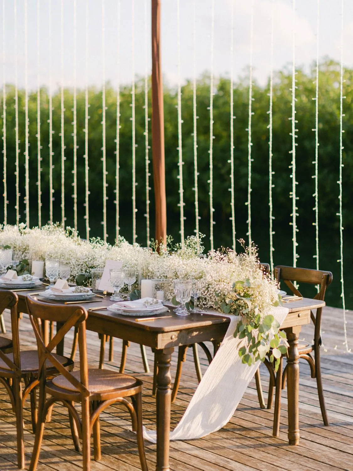 Rustic wooden wedding table decorated with baby's breath flowers and greenery. Elegant outdoor setting.