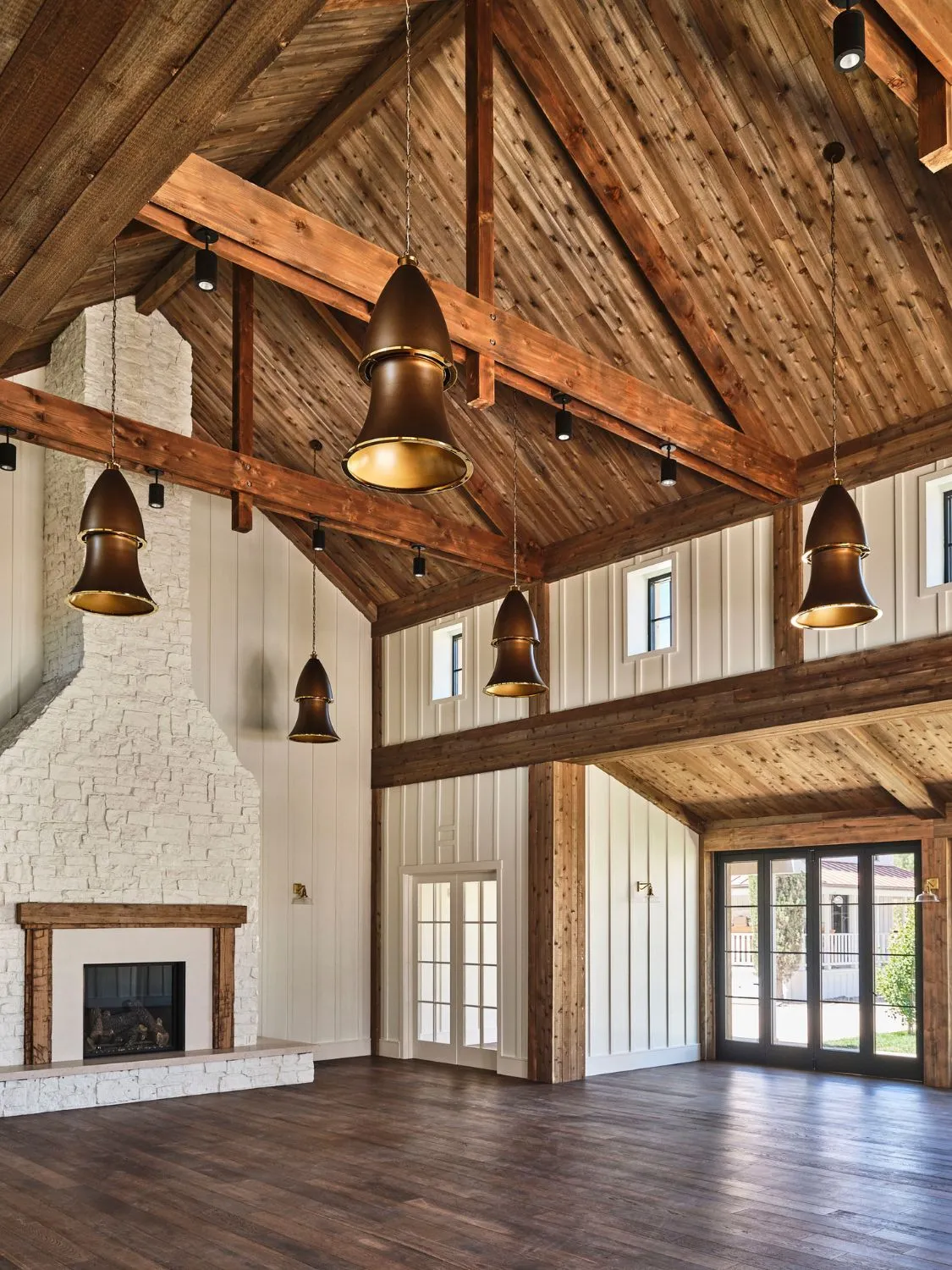 Spacious farmhouse interior with exposed wood beams, white walls, and a stone fireplace.