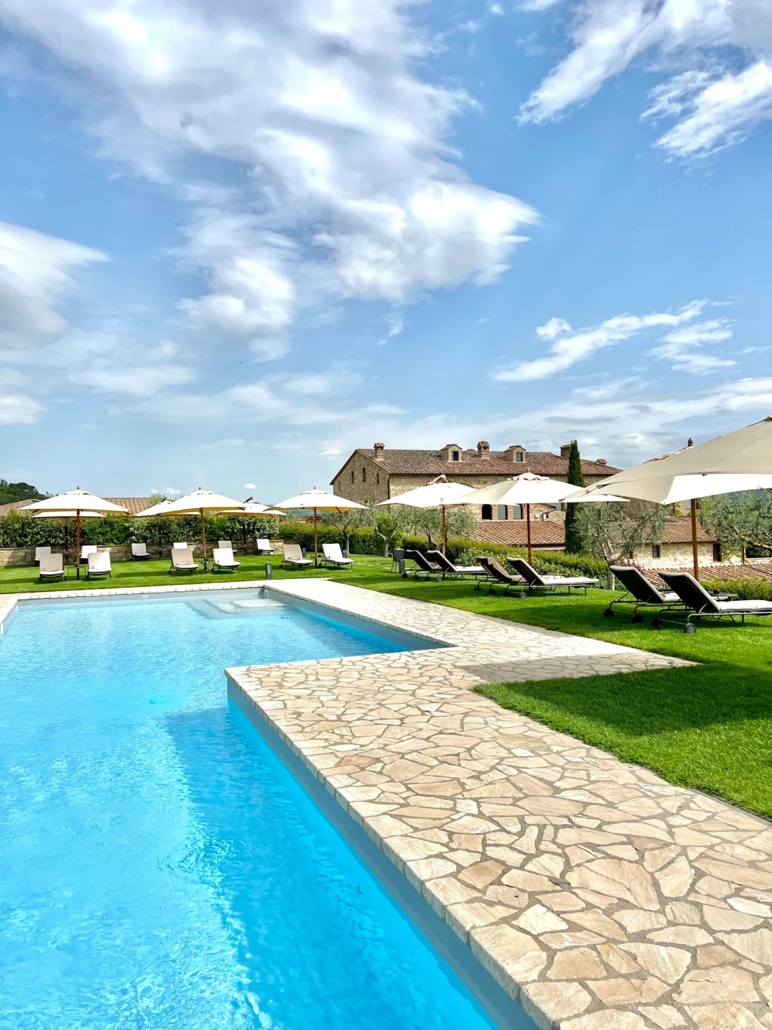 Luxury resort pool with lounge chairs and umbrellas under a blue sky.