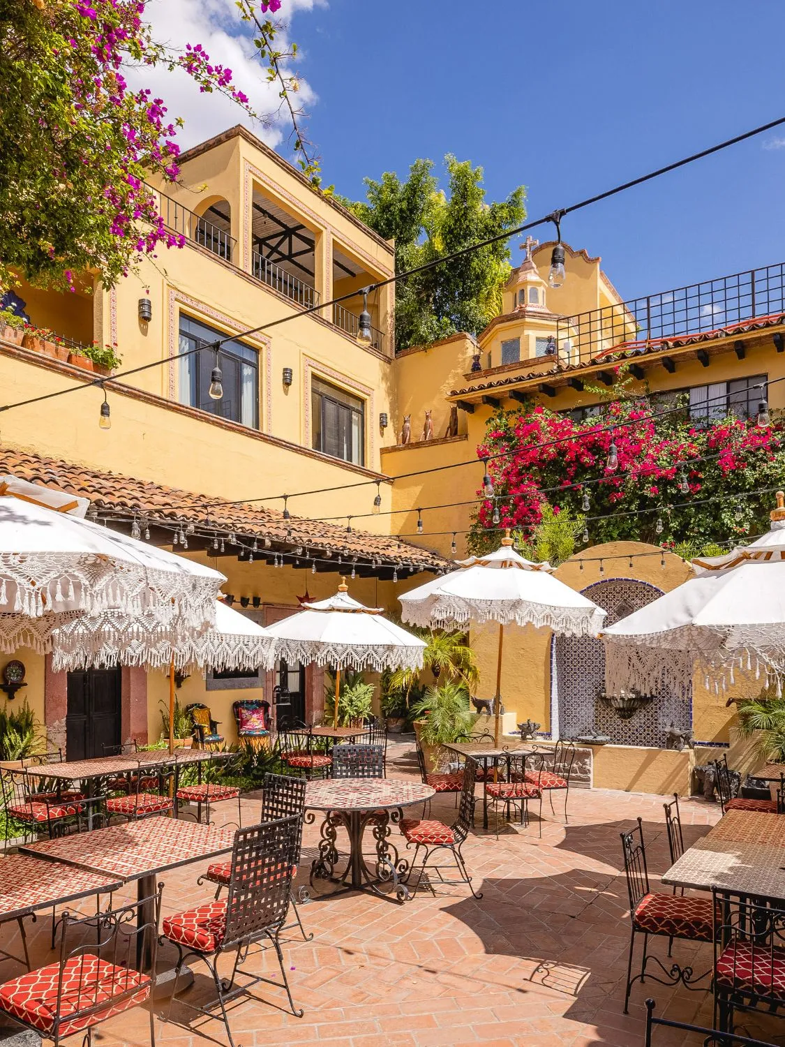 Outdoor patio restaurant with tables, chairs, and umbrellas. Beautiful Spanish-style architecture.