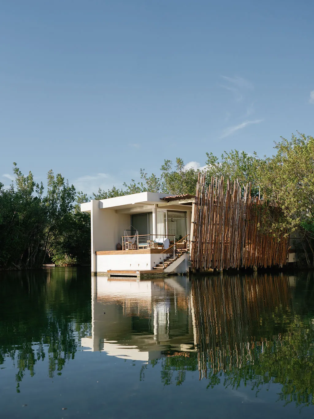 Luxury overwater bungalow with wooden privacy screen, reflecting in calm water.