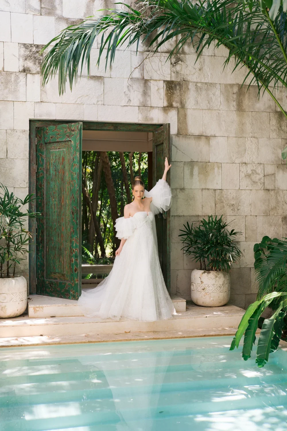 Bride in off-the-shoulder gown poses by pool for styled shoot.