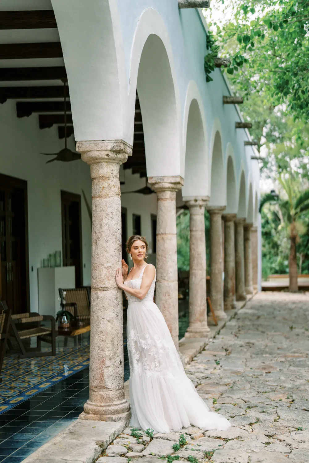 Bride in a flowing wedding gown poses under a stone archway during a styled shoot.