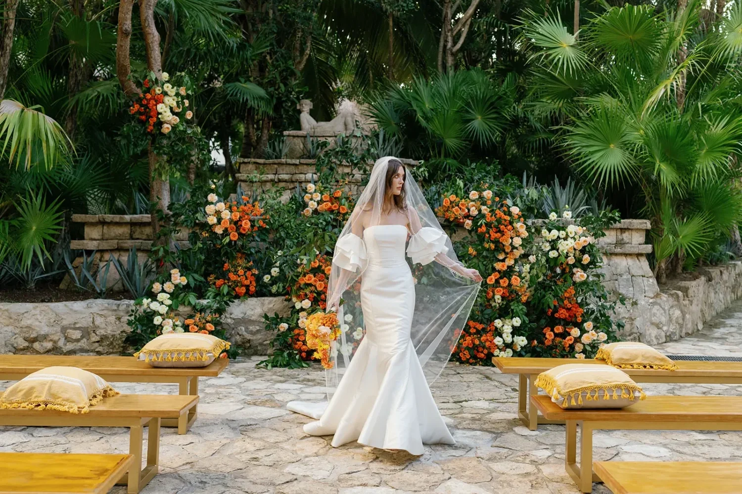 Bride in a white gown walks down the aisle toward a floral backdrop for a styled shoot.