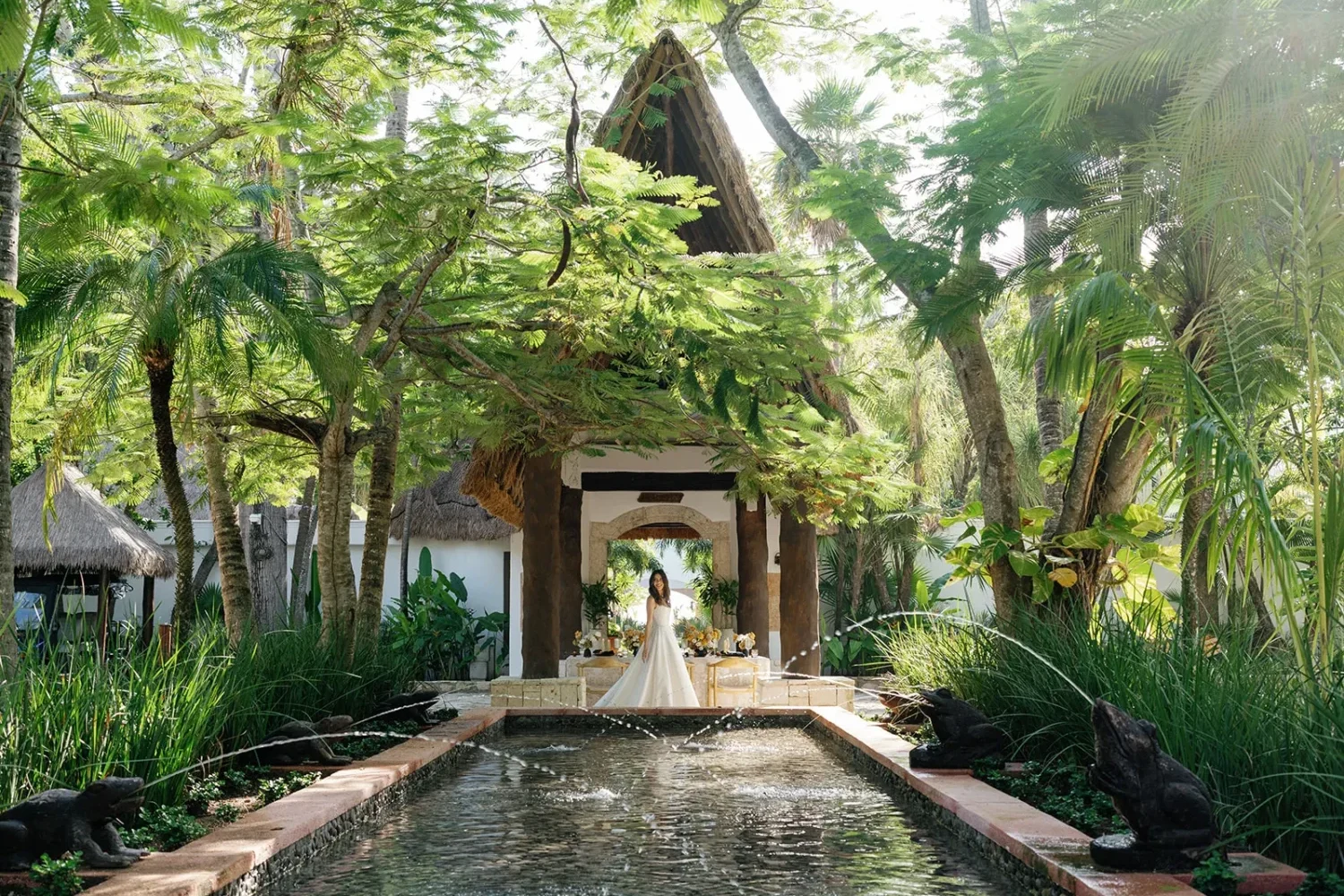 Bride in a flowing wedding gown poses in a lush tropical garden setting for a styled shoot.
