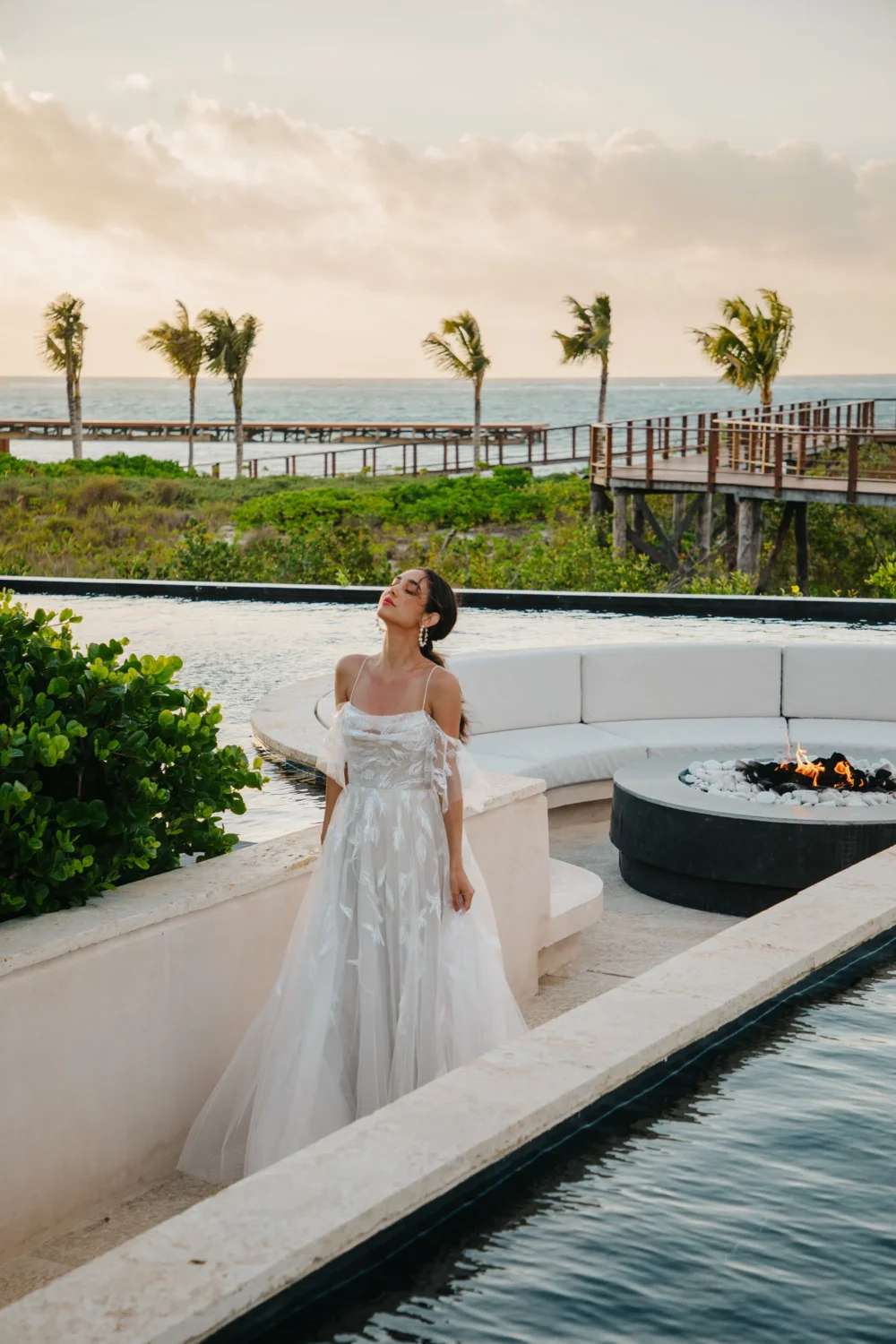 Bride in a white lace gown poses by a resort pool during a styled shoot.