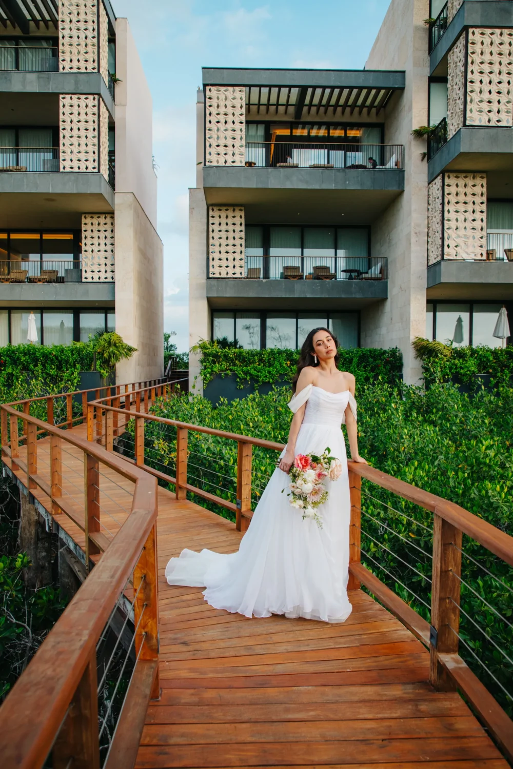 Bride in white gown holds bouquet on wooden walkway, styled shoot.
