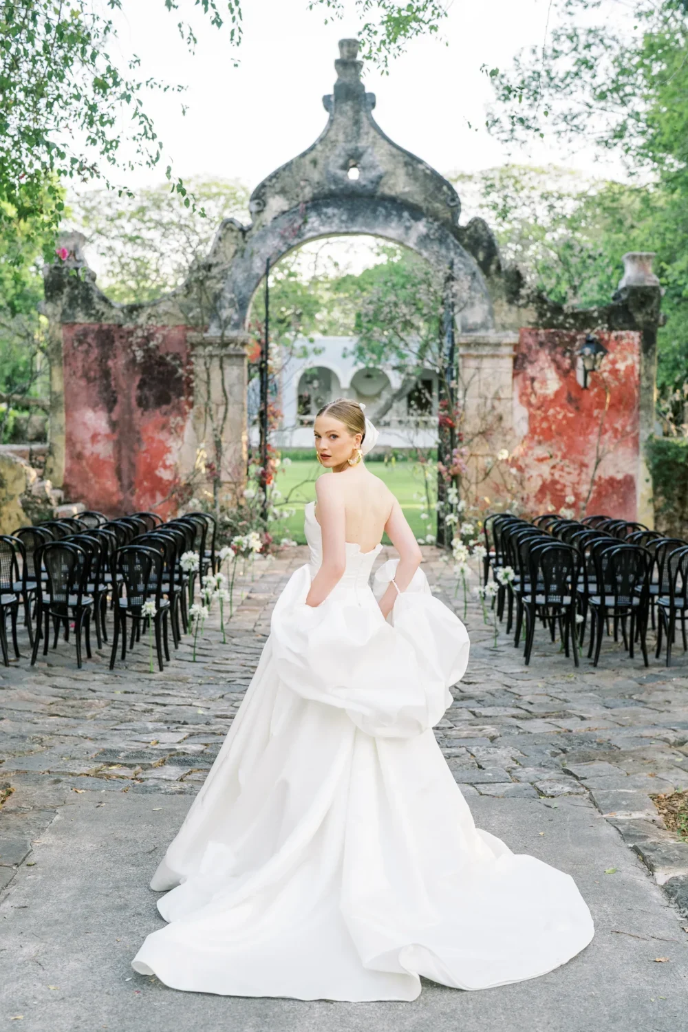 Bride in a white gown at a styled shoot, posing outdoors at a stone archway.