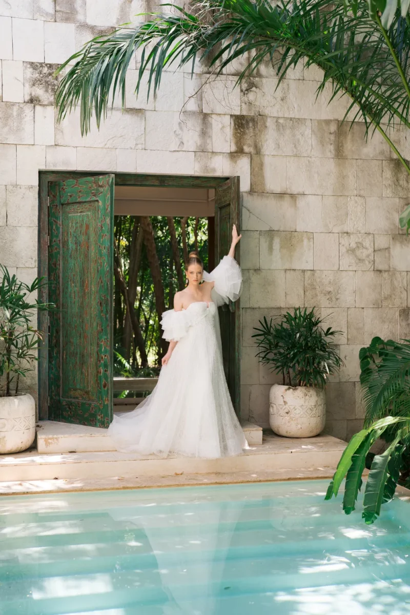 Bride in off-the-shoulder gown poses by pool for styled shoot.
