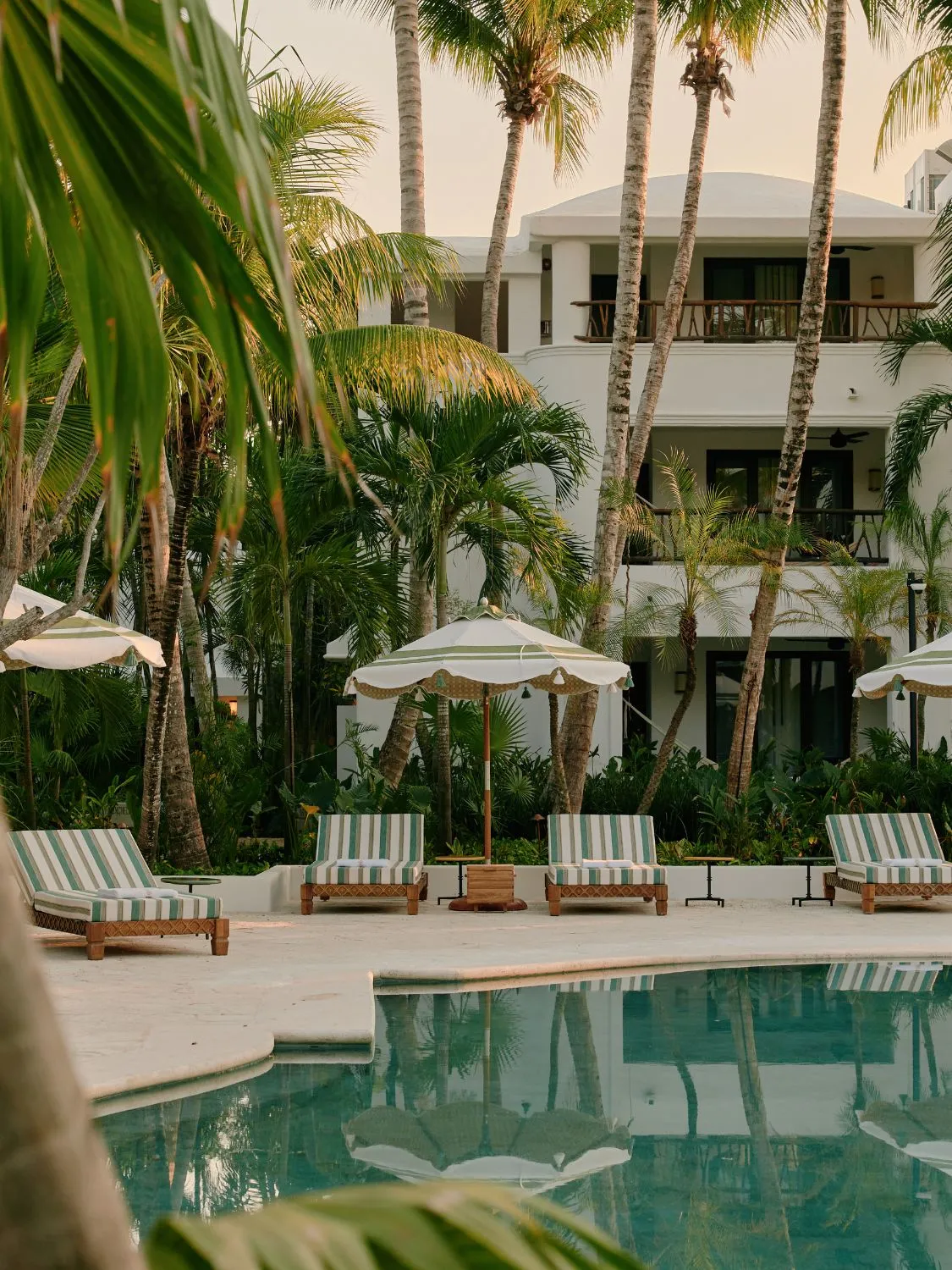 Luxury resort pool with striped lounge chairs and palm trees.