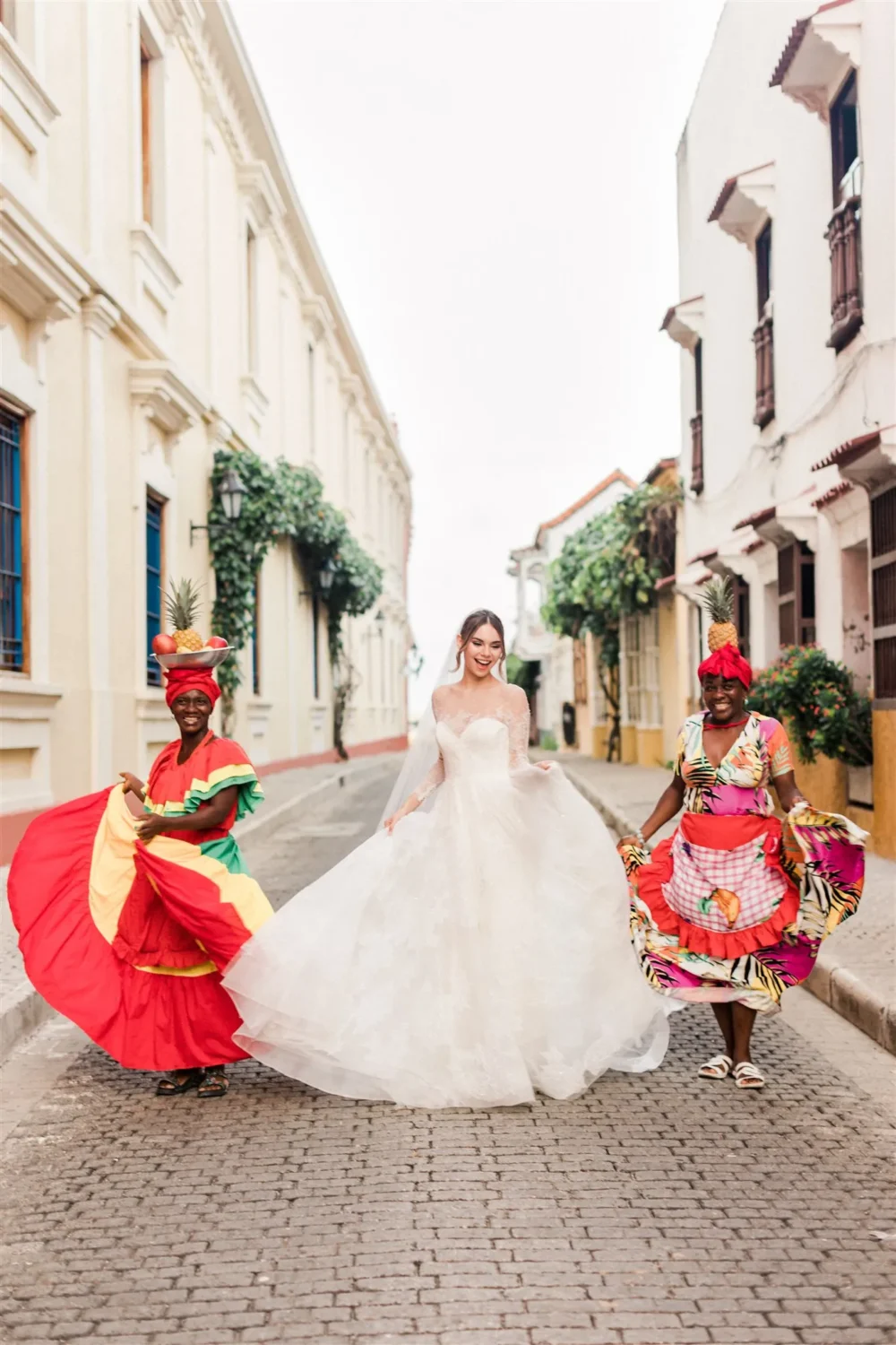 Bride in a flowing wedding gown with two women in colorful traditional dresses, styled shoot.