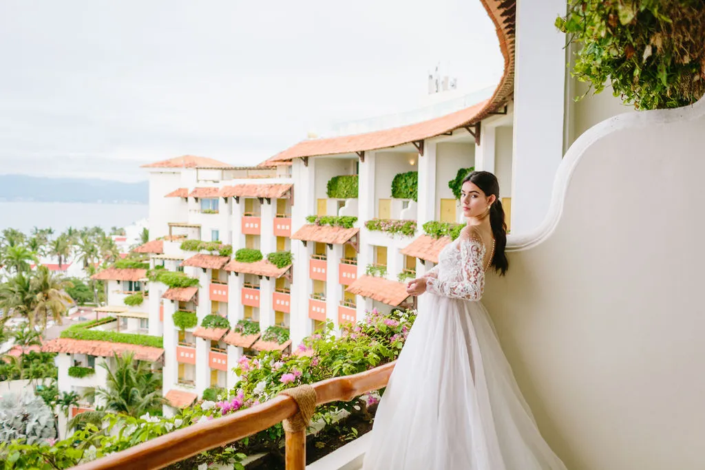 Bride in lace wedding gown on hotel balcony overlooking ocean; styled shoot