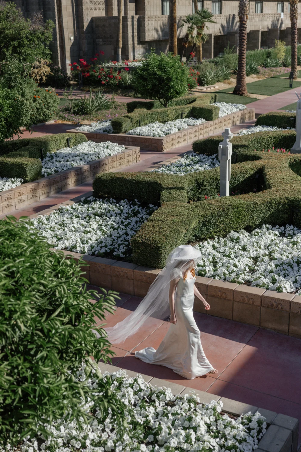 Bride in white gown and hat walks through a garden for a styled shoot.