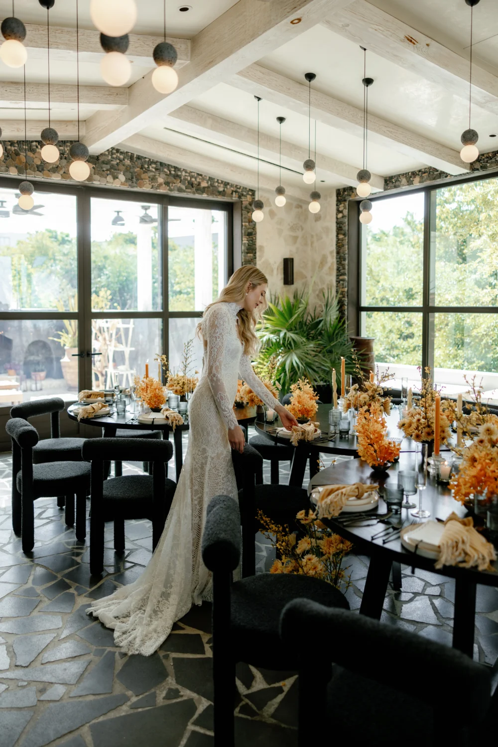 Bride in lace wedding gown setting table for styled shoot with autumnal floral arrangements.