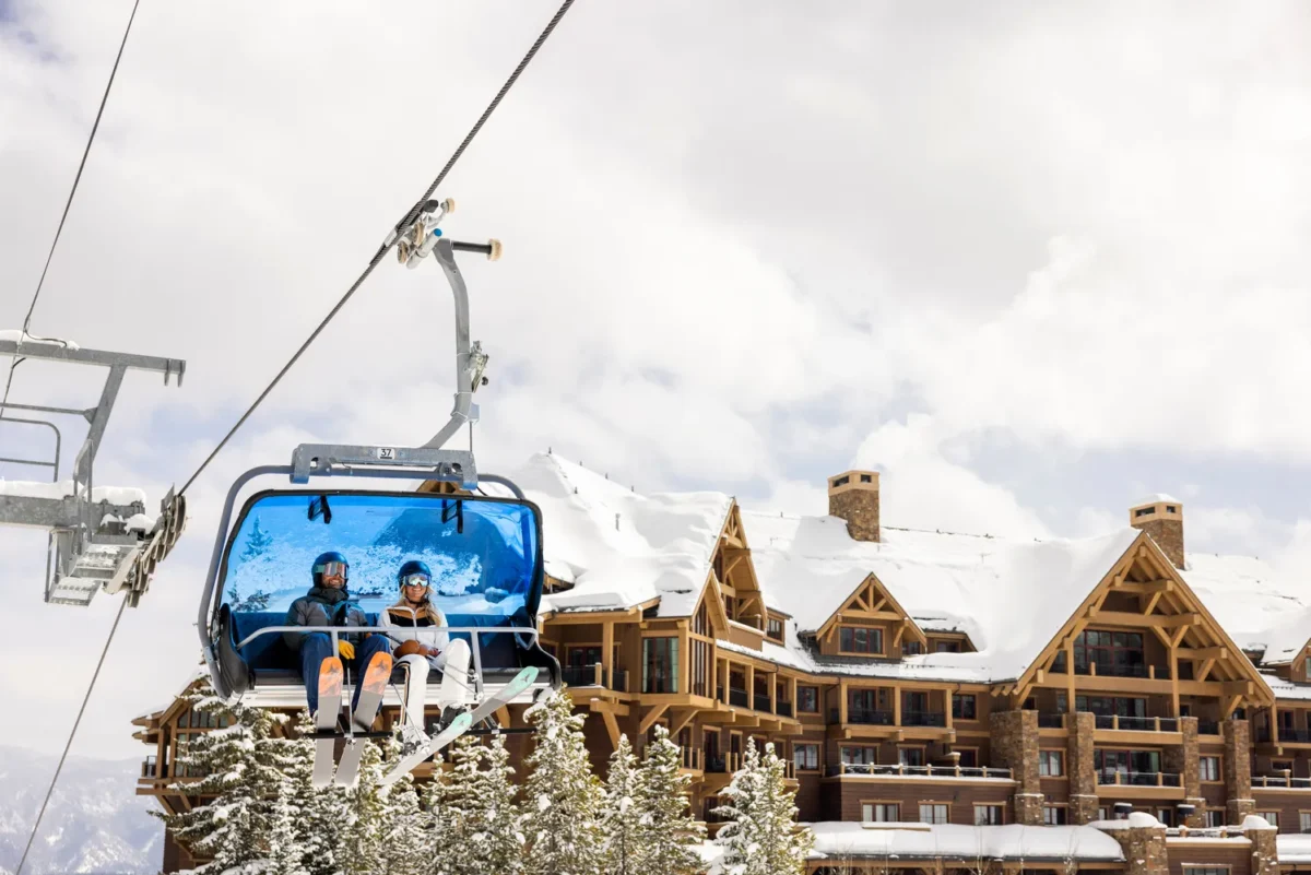 Couple on a ski lift at Montage Big Sky, a Montana wedding venue, with snow-covered building.