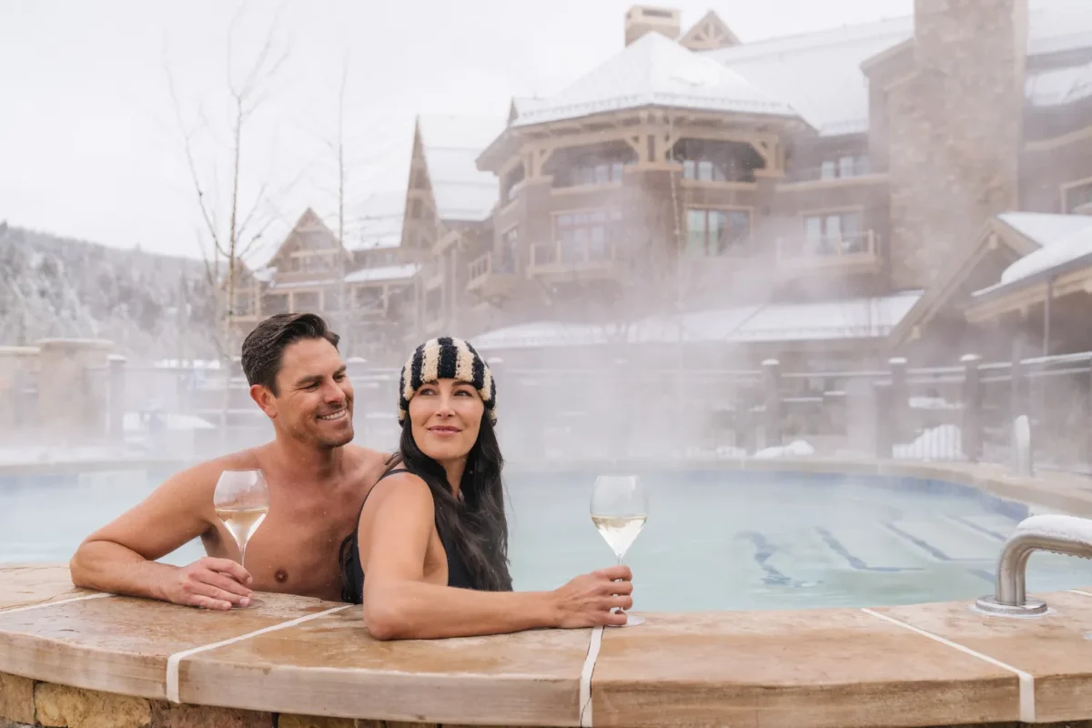 Couple relaxing in a hot tub at Montage Big Sky, enjoying wine with a snowy backdrop