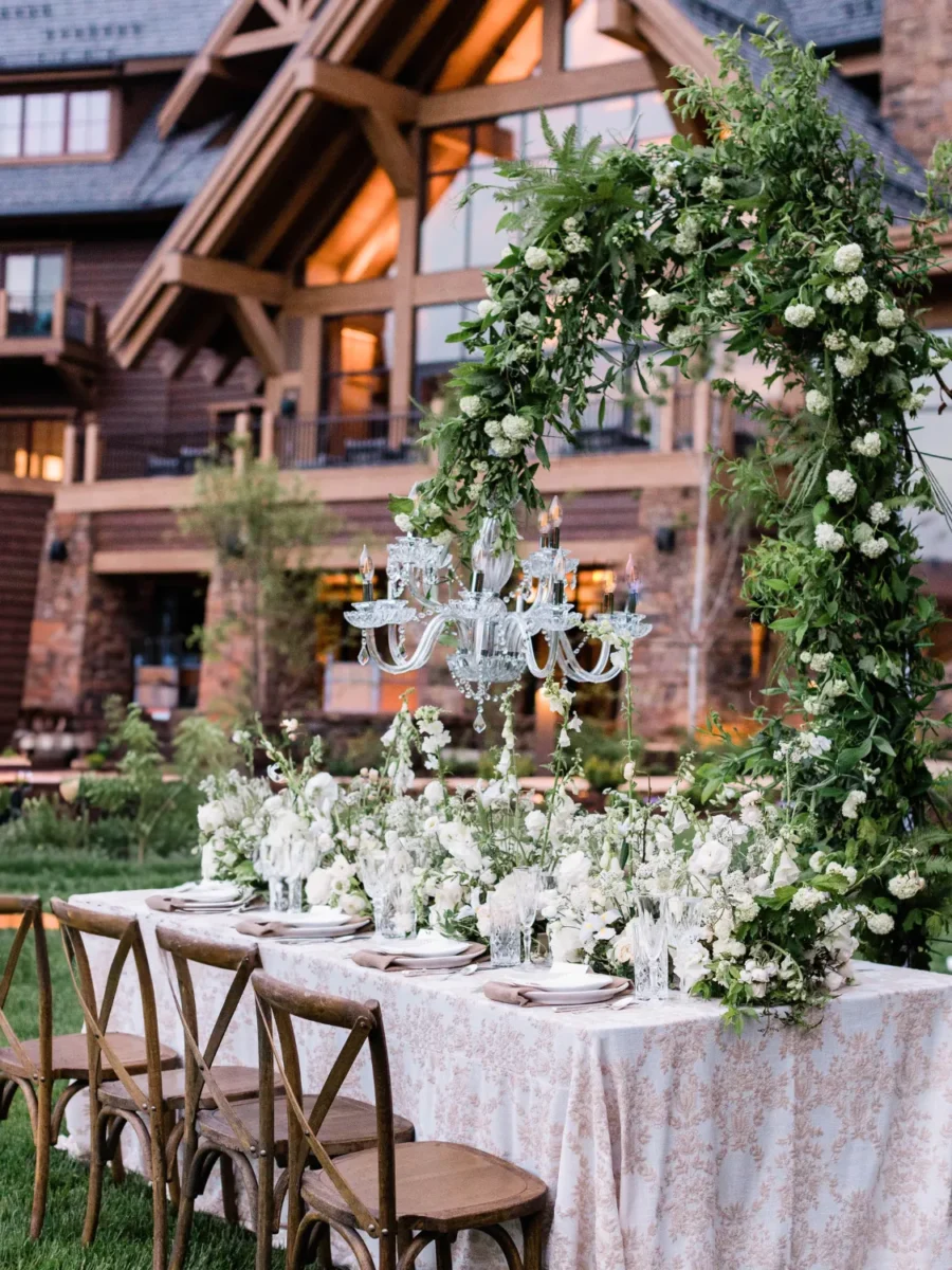 Elegant mountain wedding reception table with floral arch and chandelier.