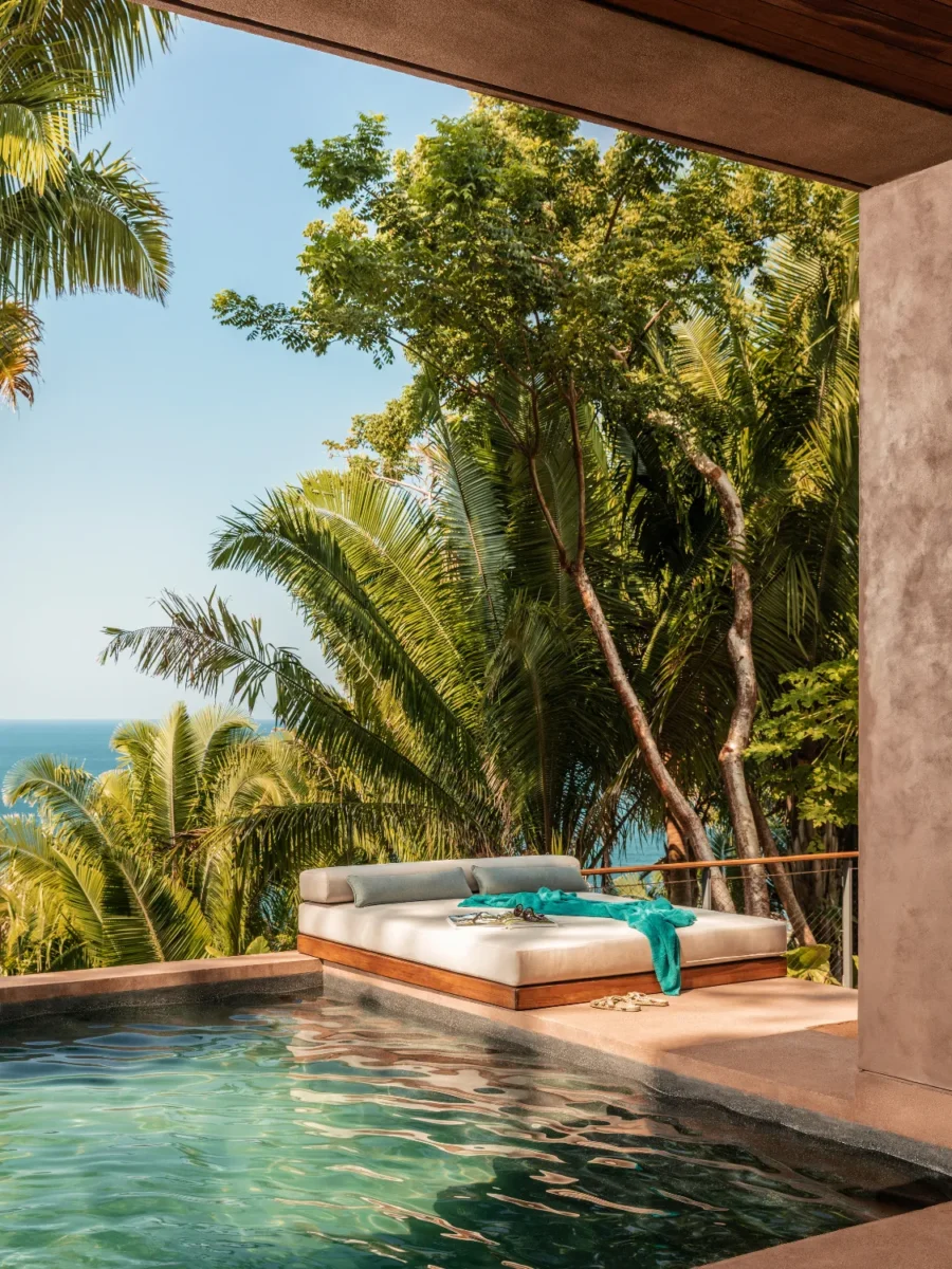 Luxury villa with pool and daybed overlooking tropical trees and ocean view.