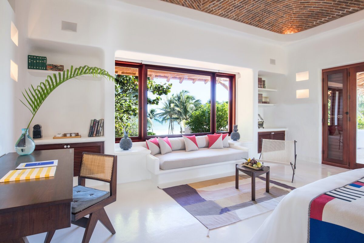 Bright luxury hotel room design with a window seat overlooking a tropical beach.