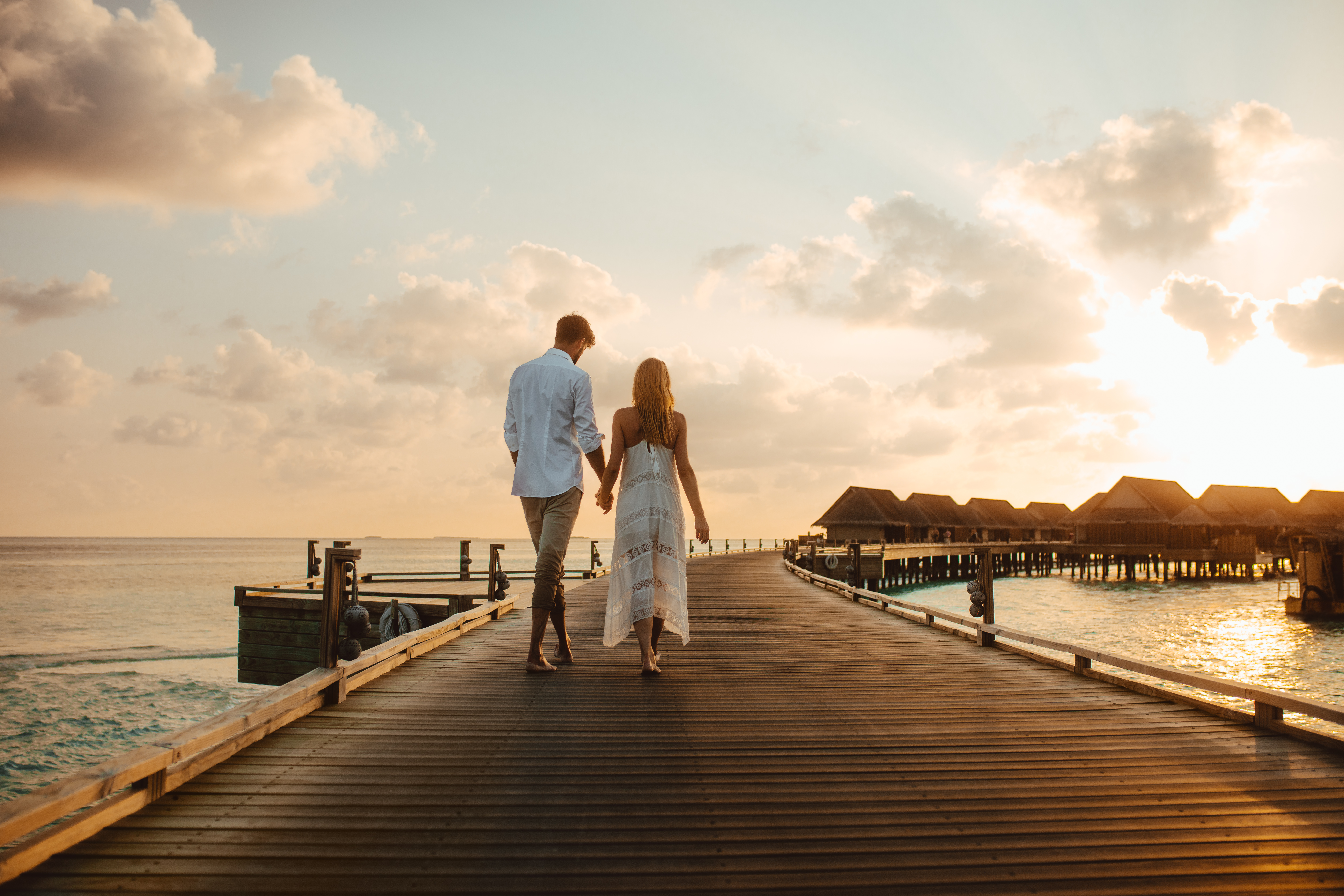 Couple walking hand-in-hand on a pier towards overwater bungalows at sunset, perfect for luxury honeymoons 2026.