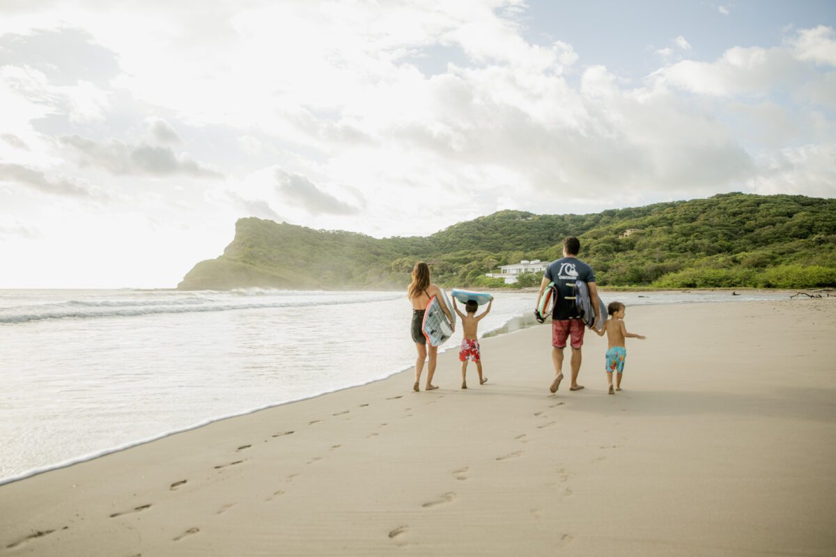 Family walking on a Rancho Santana beach with surfboards and boogie boards.