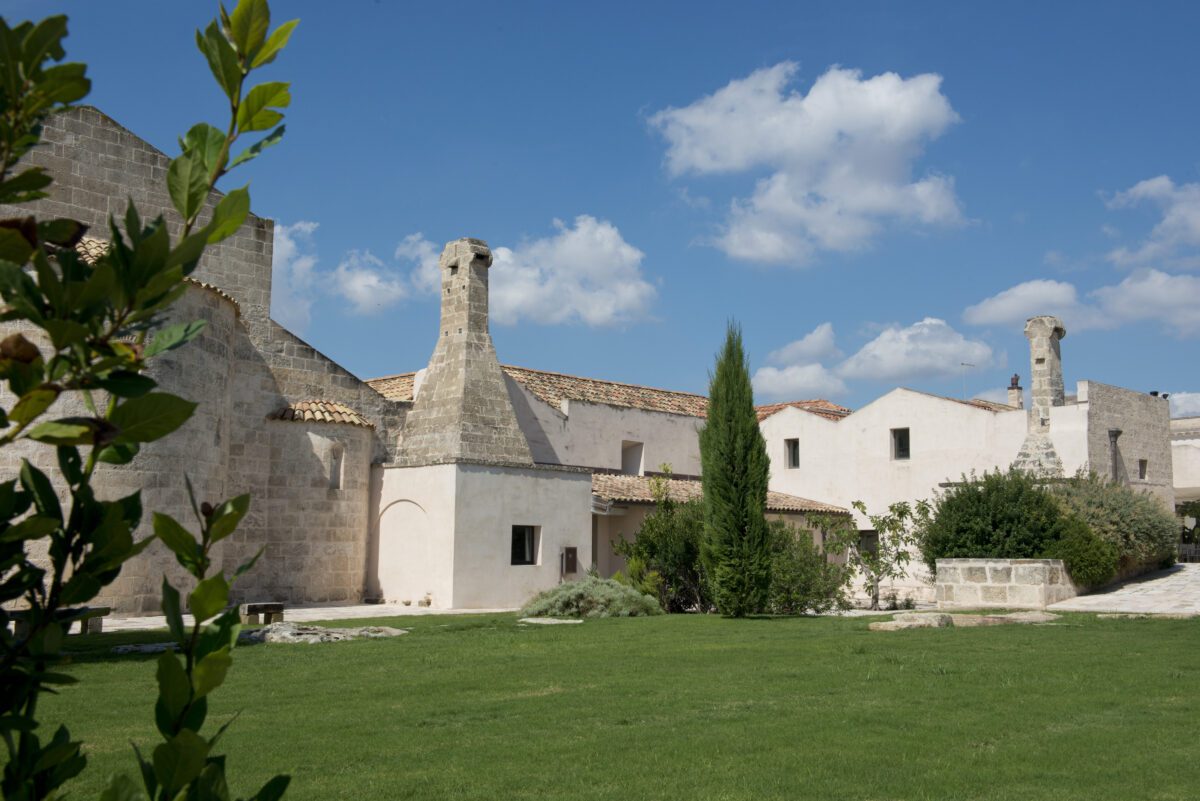Relais Histò Hotel & SPA courtyard view with stone buildings, green lawn, and blue sky.