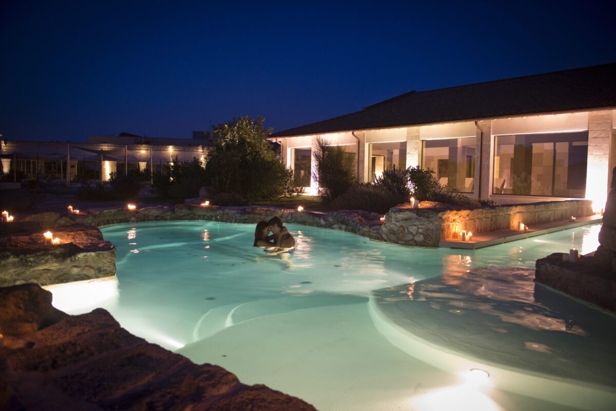 Couple in illuminated pool at Relais Histò Hotel & SPA at night.