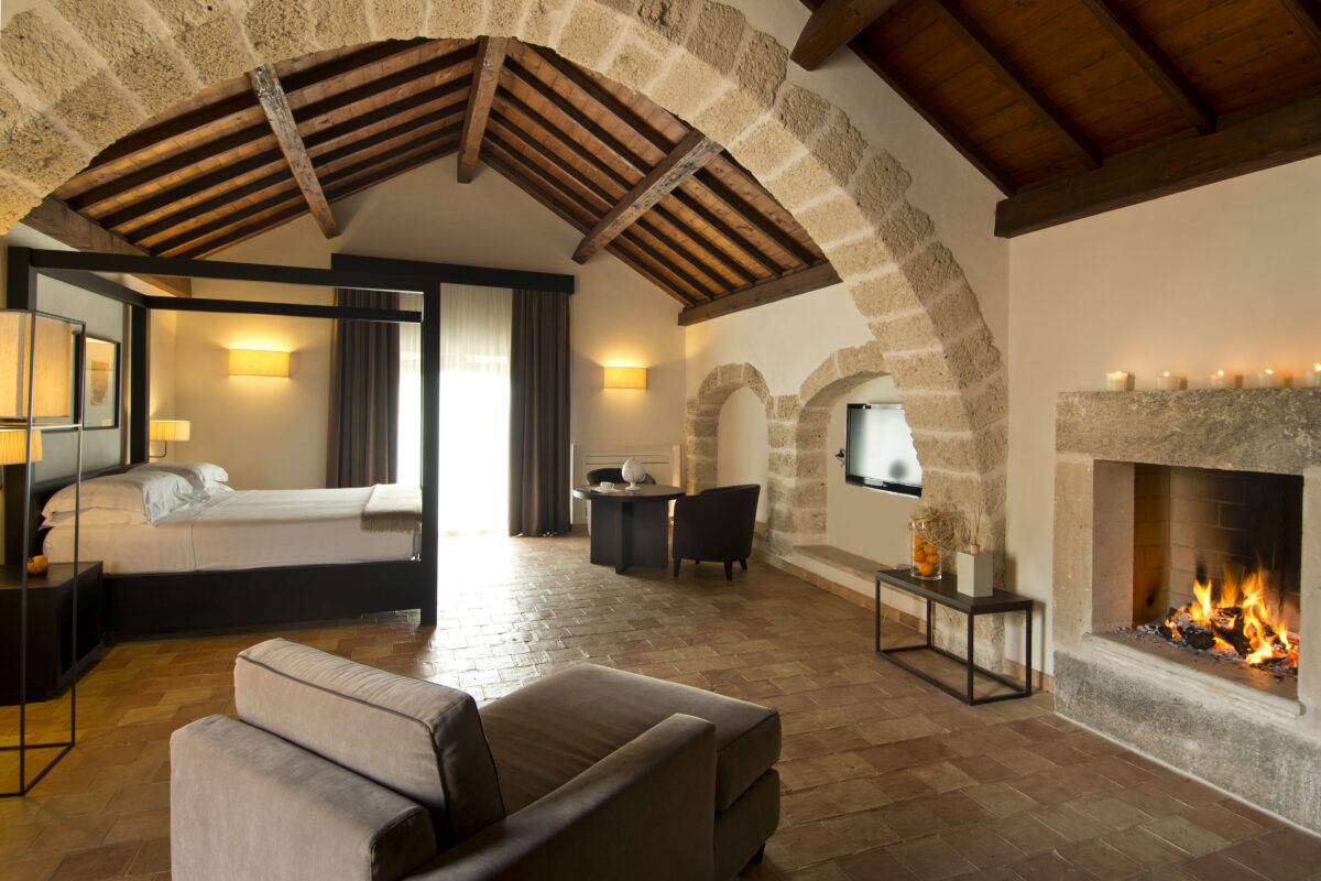 Luxurious Relais Histò hotel room with stone arches, wood beams, fireplace, and four-poster bed.
