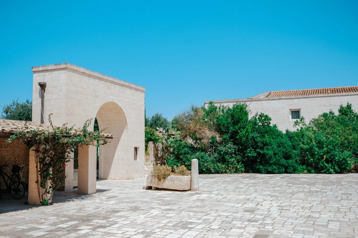 Relais Histò Hotel courtyard with stone architecture, greenery, and bright blue sky.