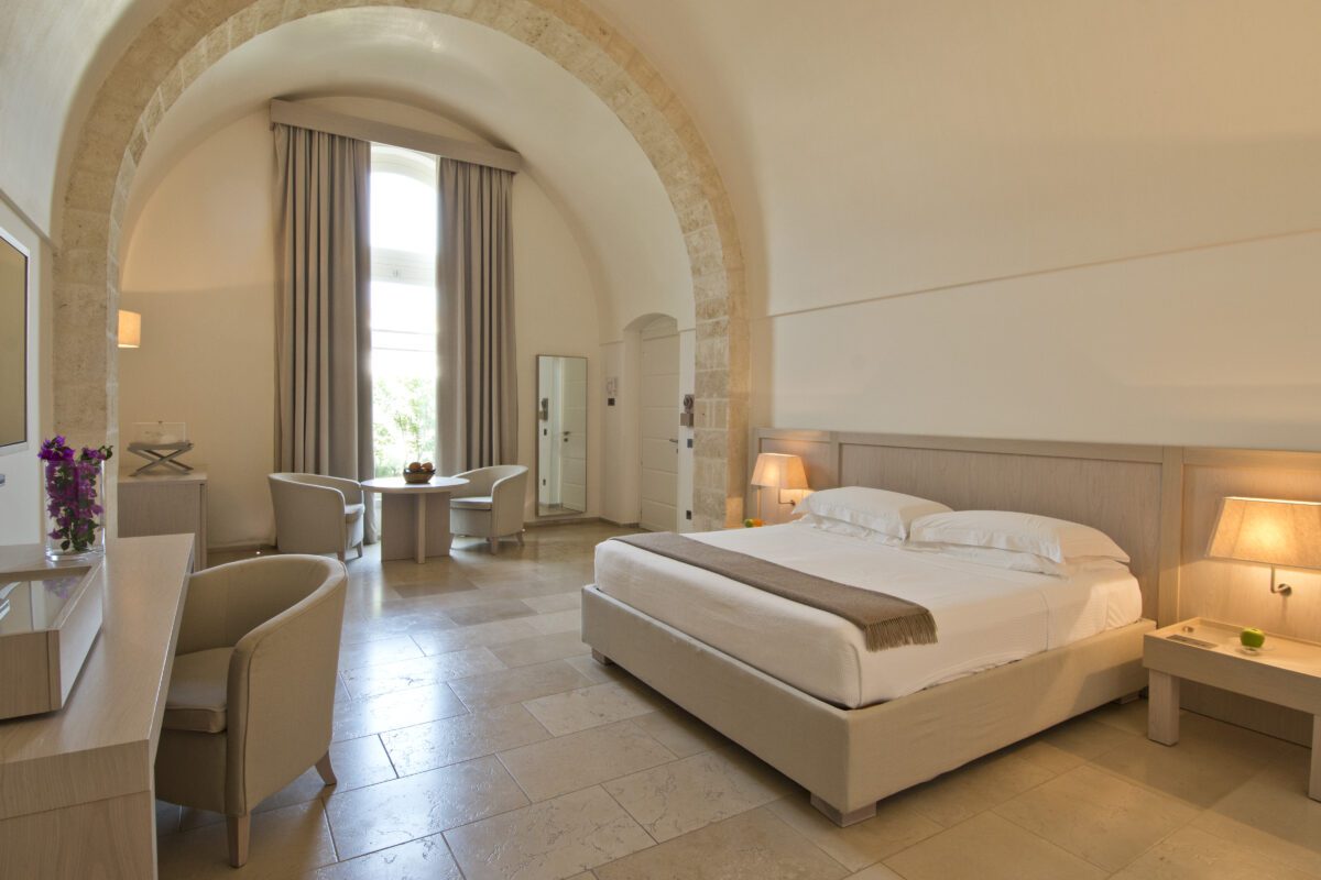Relais Histò hotel room with stone arch, king bed, seating area, and neutral decor.