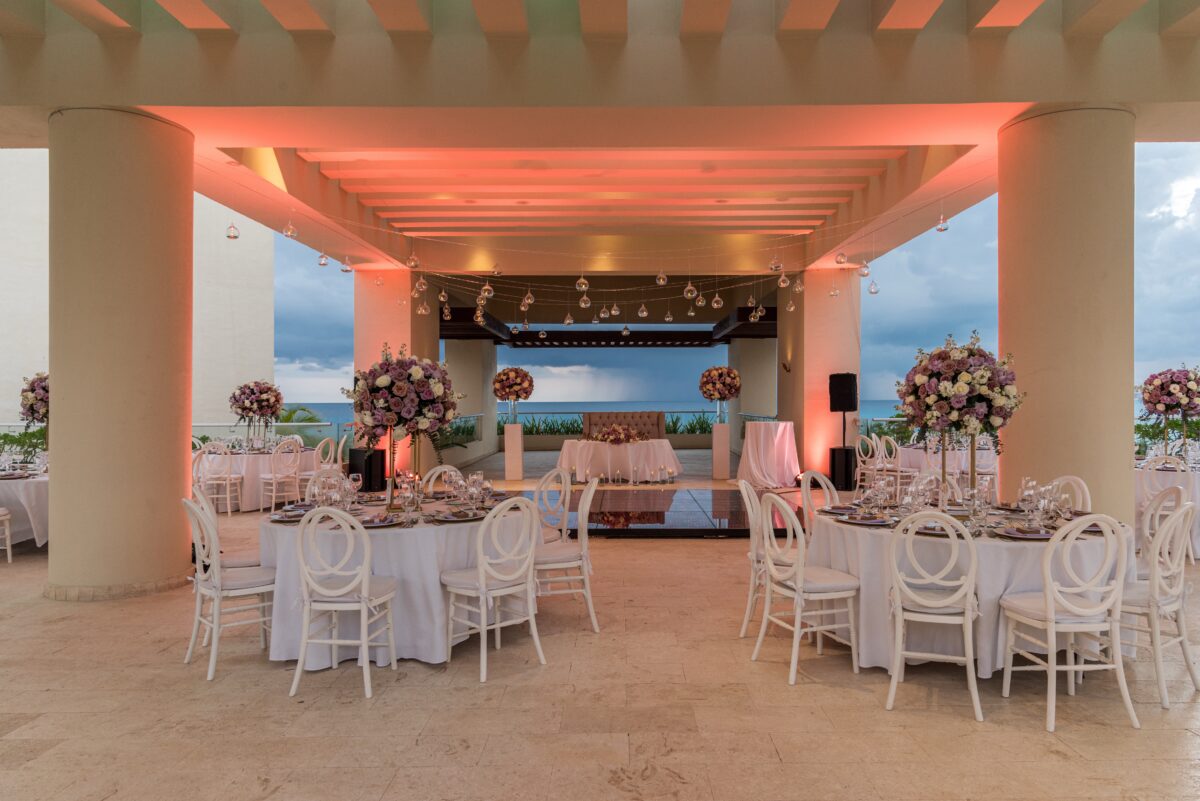 Luxury wedding venue in Cancun: Elegant reception setup with white tables, chairs, and floral centerpieces overlooking the ocean.