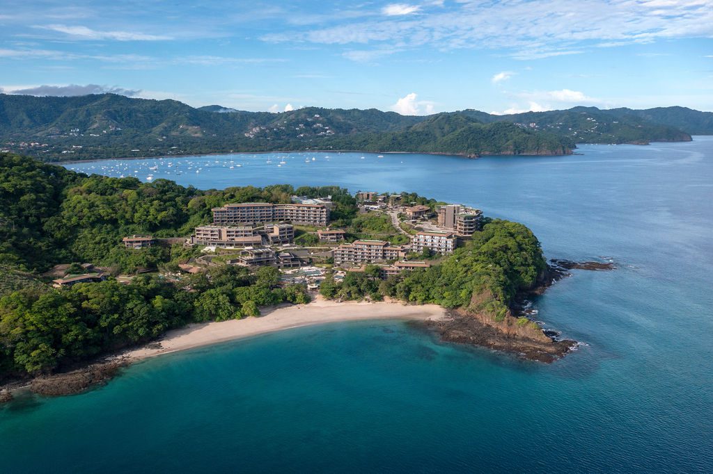Aerial view of the Waldorf Astoria Costa Rica resort on a lush peninsula with a sandy beach and turquoise water.