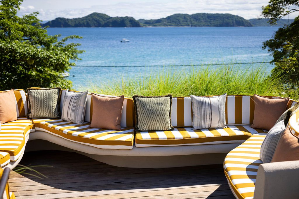 Outdoor seating at Waldorf Astoria Costa Rica with ocean view. Striped cushions and decorative pillows.
