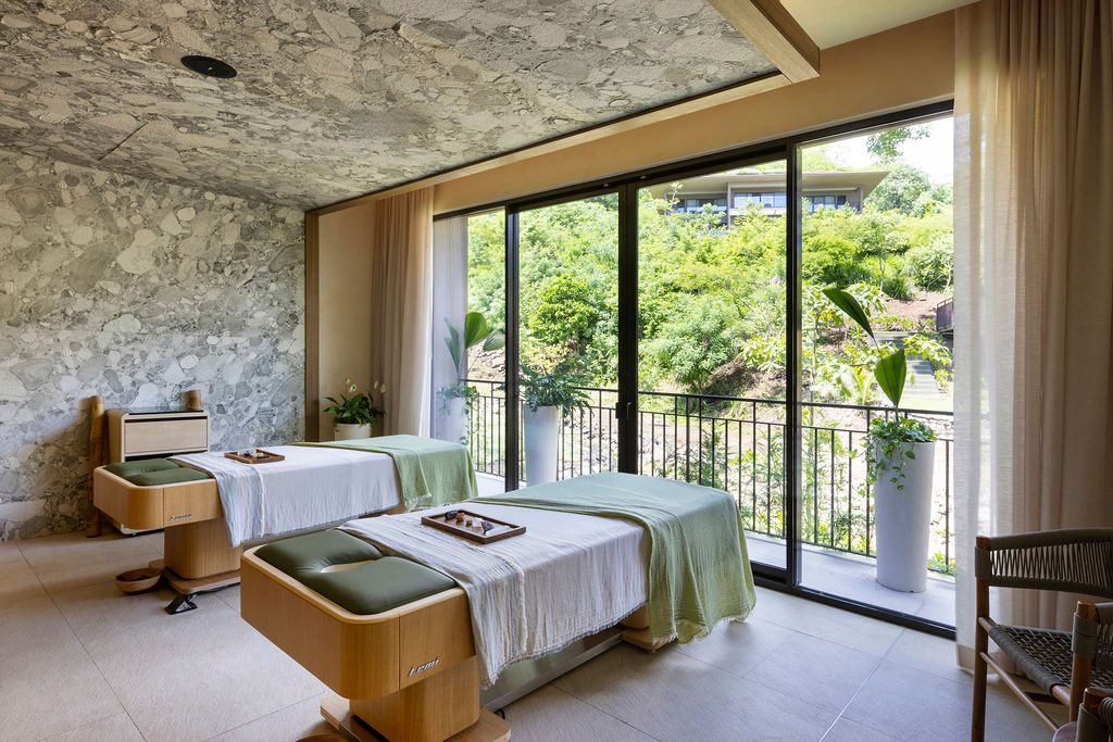 Waldorf Astoria Costa Rica spa room with two massage tables and a view of lush greenery.