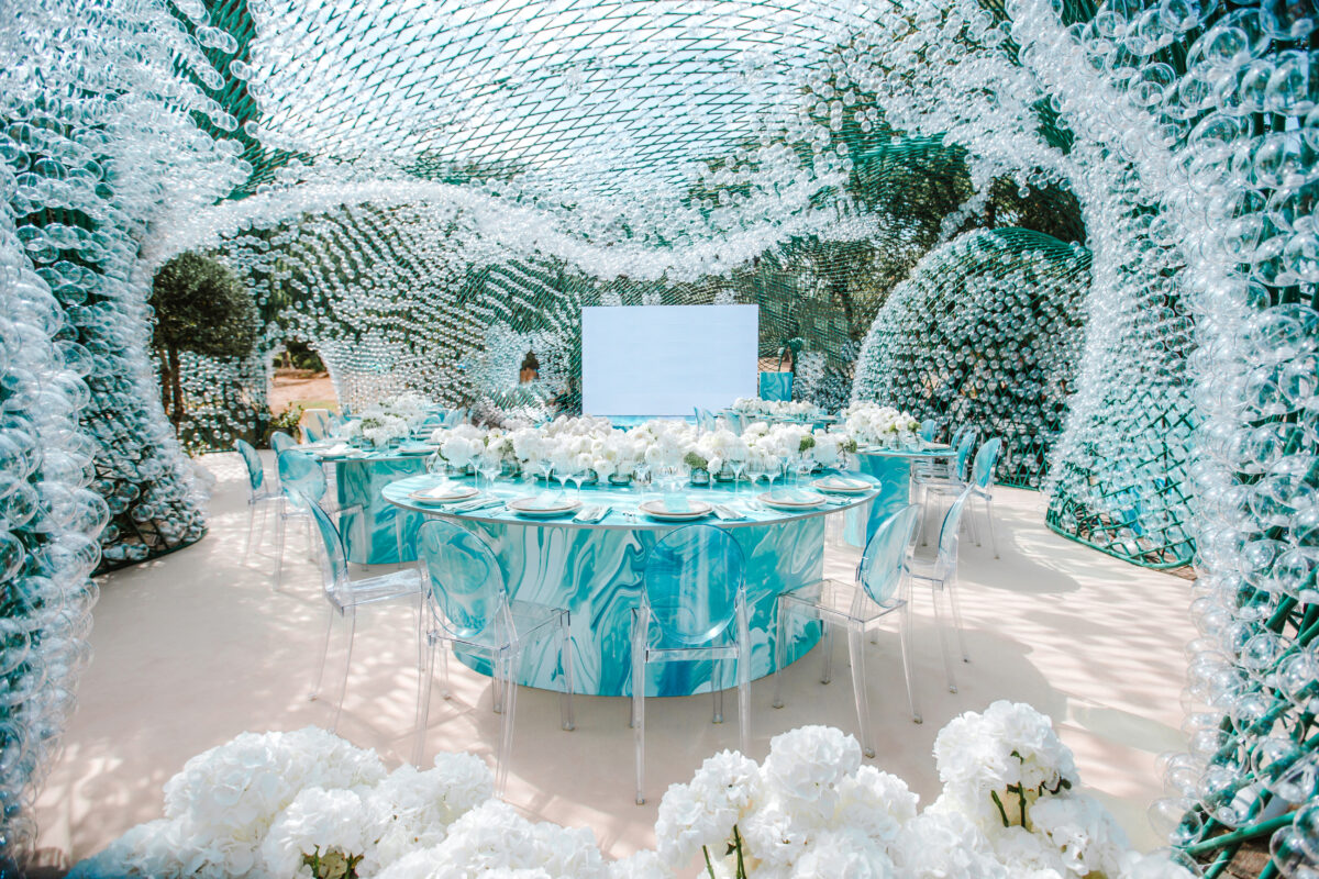 Luxury wedding setup at COMO Le Beauvallon, Saint-Tropez. Round tables with white florals under a unique glass structure.