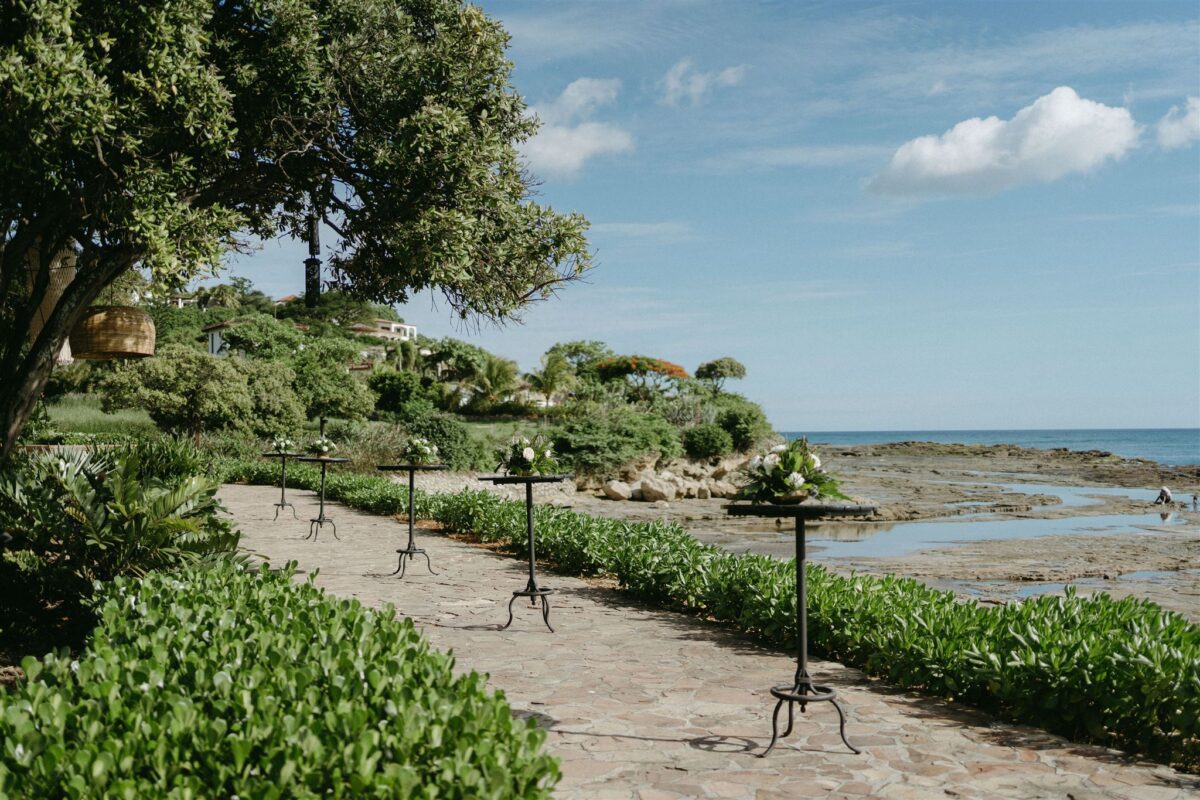 Rancho Santana wedding setup on a stone path by the ocean, with floral arrangements on black stands.