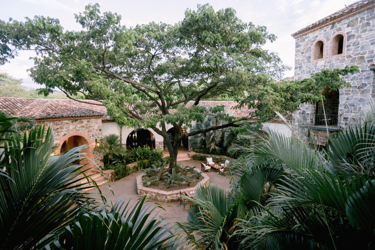 Courtyard with a large tree surrounded by rustic buildings at Rancho Santana