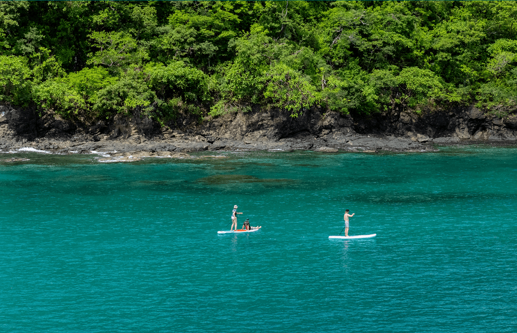 Paddleboarding in turquoise waters near lush coastline, Waldorf Astoria Costa Rica.