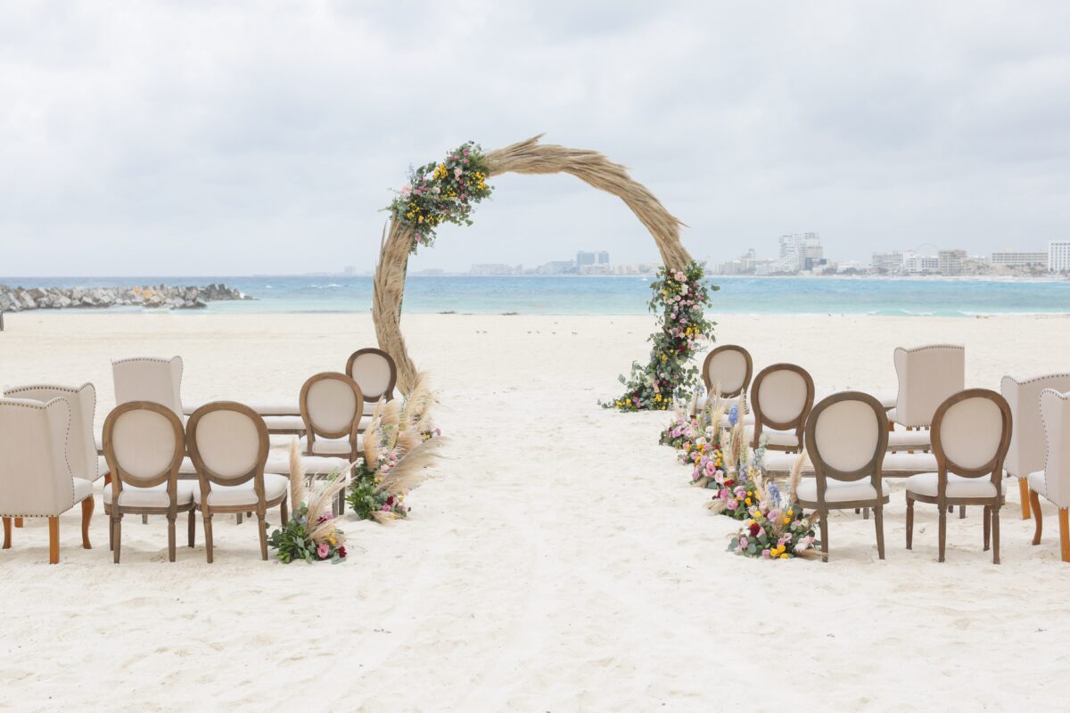 Beach wedding setup at Hyatt Ziva Cancun. Circular arch with flowers, chairs on white sand. Luxury wedding venue.