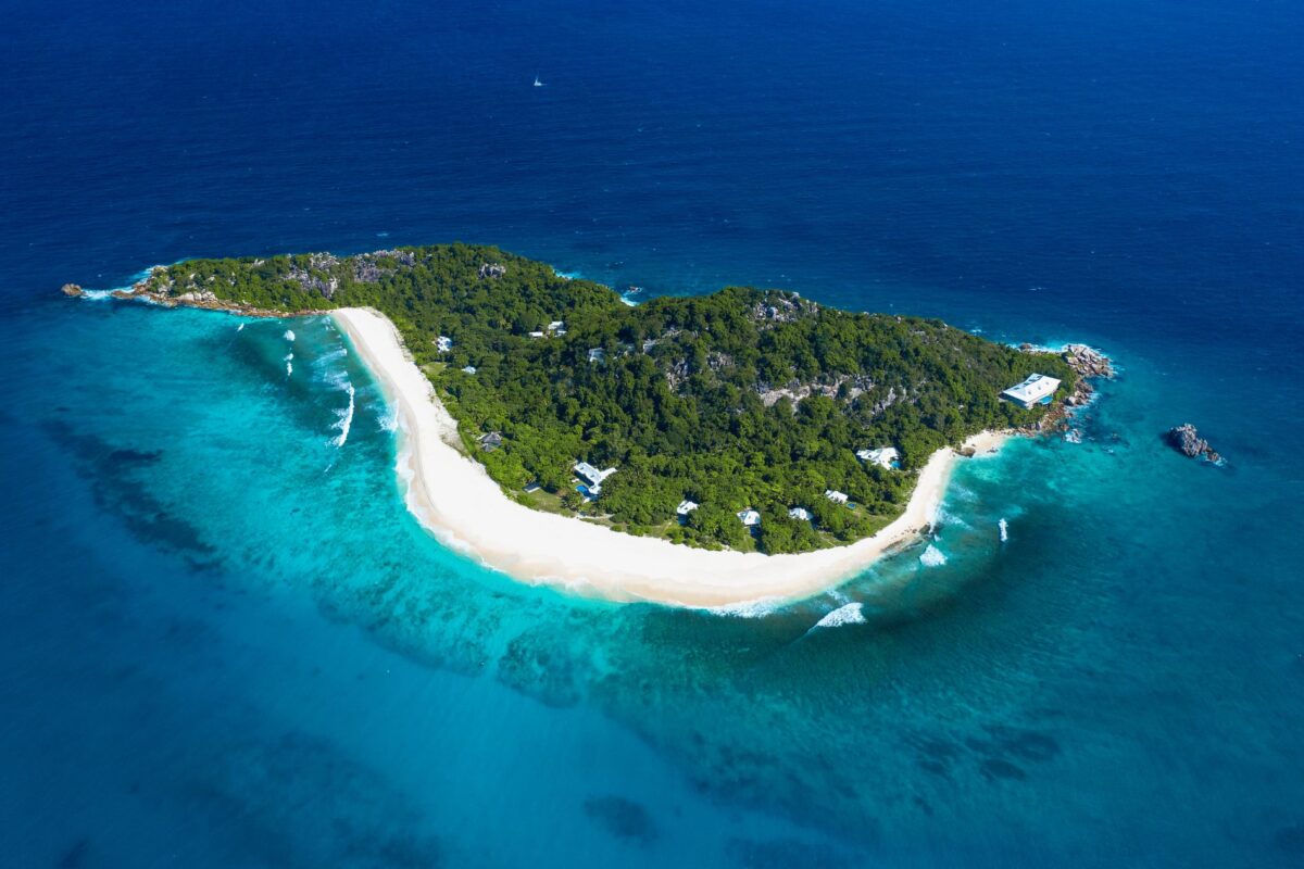 Aerial view of a tropical island with white sand beach and luxury villa rentals nestled in lush greenery.