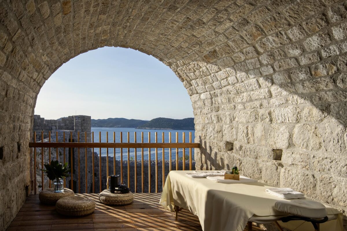 Massage table with ocean view inside a stone archway. Luxury villa rentals offer stunning views.