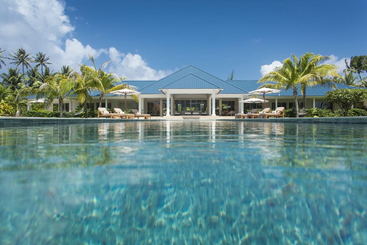 Luxury villa rental with a blue roof, palm trees, and a swimming pool.