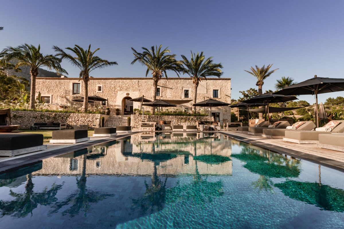 Luxury villa rentals: Pool reflecting the stone villa with palm trees and lounge chairs.
