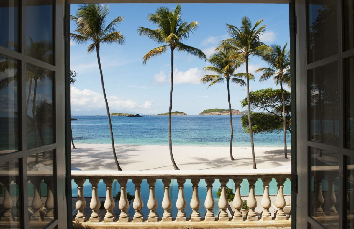 View of a tropical beach with palm trees from a luxury villa rental balcony.