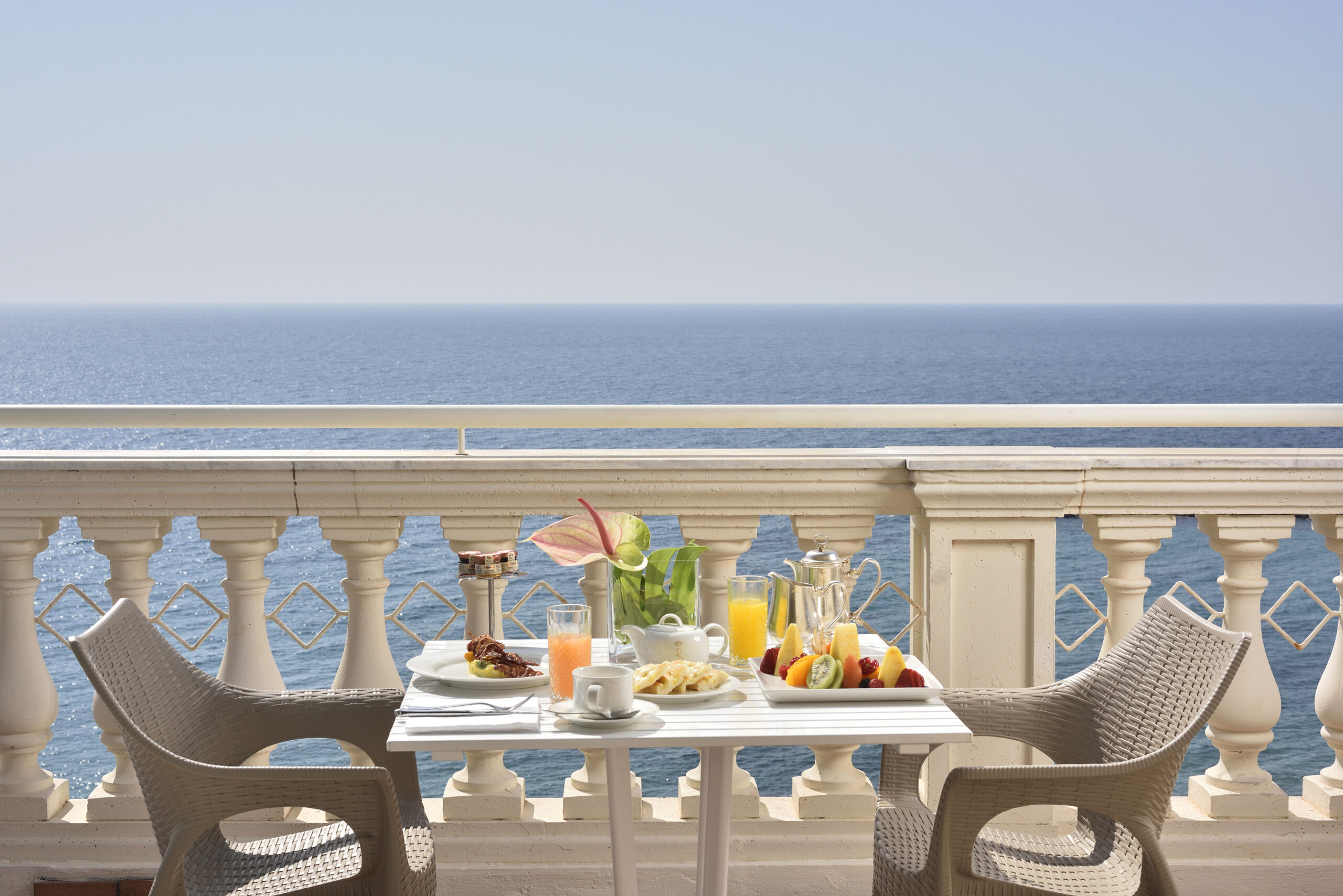 Breakfast with ocean view at Royal Hotel Sanremo balcony. Fruit, juice, pastries, and coffee.