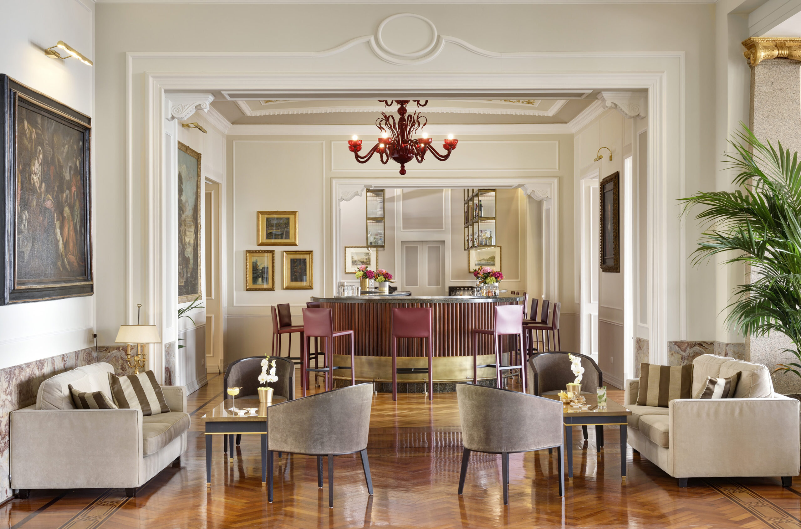 Royal Hotel Sanremo bar area with elegant seating, a red chandelier, and parquet flooring.